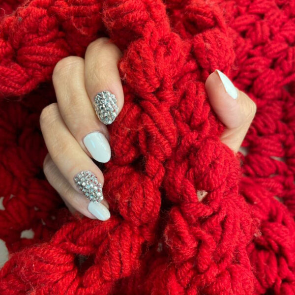 Refect Beauty Yolo Nail Crystals Struss on white manicured nails against a textured red knit background