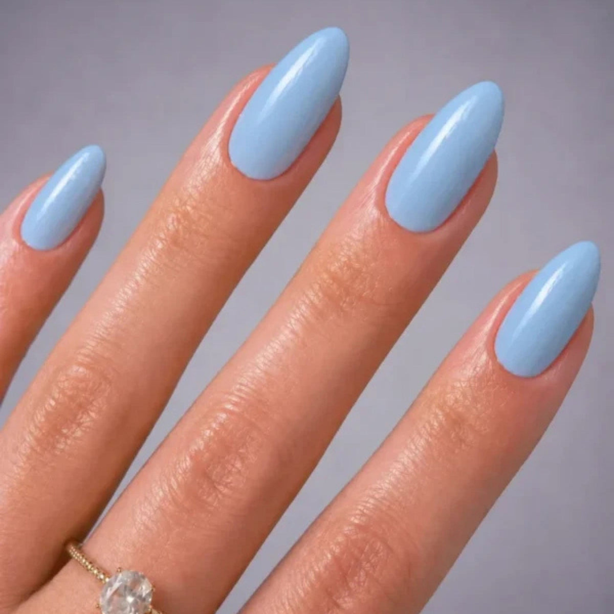 Refect Beauty Yolo pastel blue nail polish on almond-shaped nails with a glossy finish and a delicate gold ring.