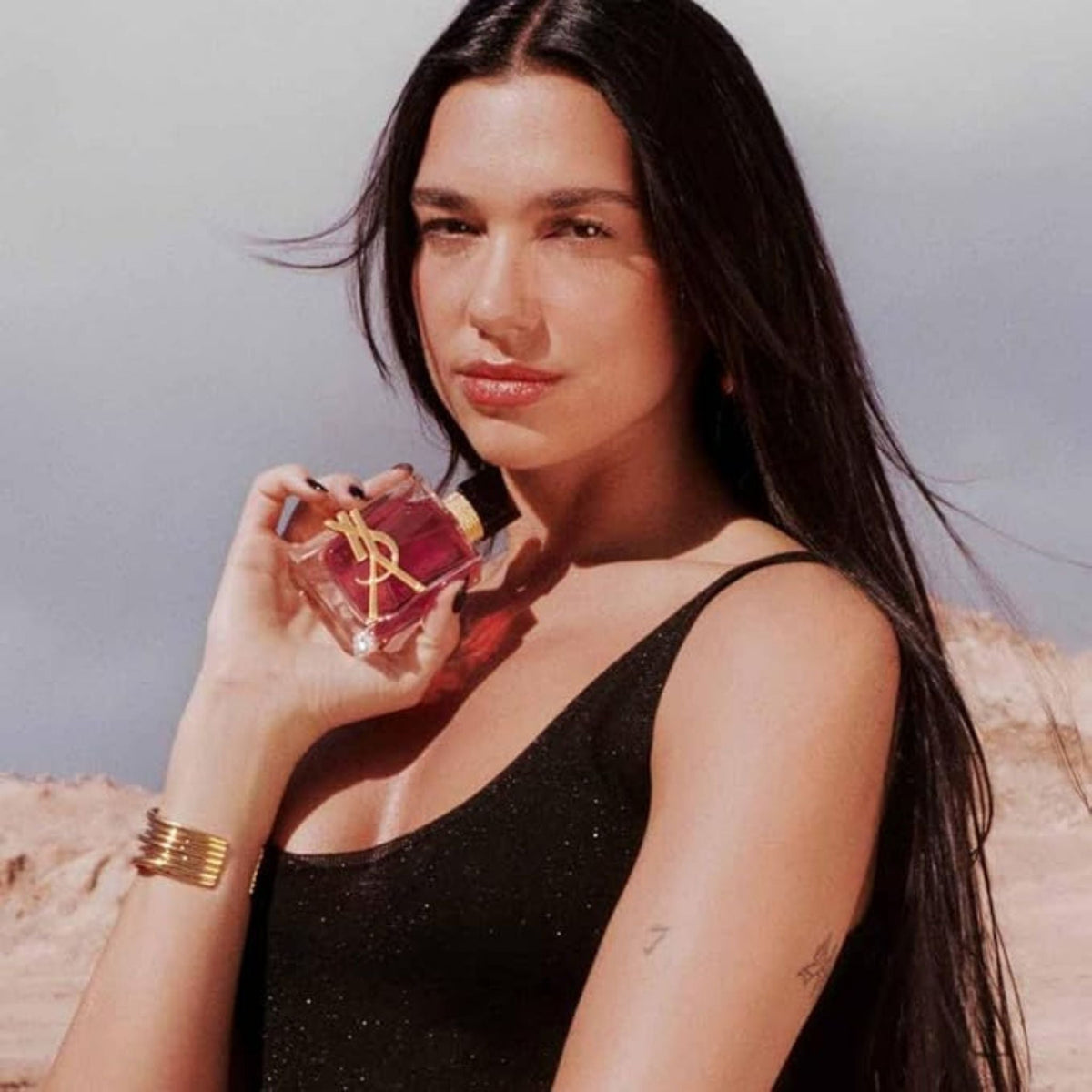 Refect Beauty model holding a bottle of Yves Saint Laurent Libre Berry Crush perfume in a desert landscape
