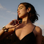 Refect Beauty model holding Yves Saint Laurent Libre Le Parfum bottle with gold YSL logo against a sunset sky